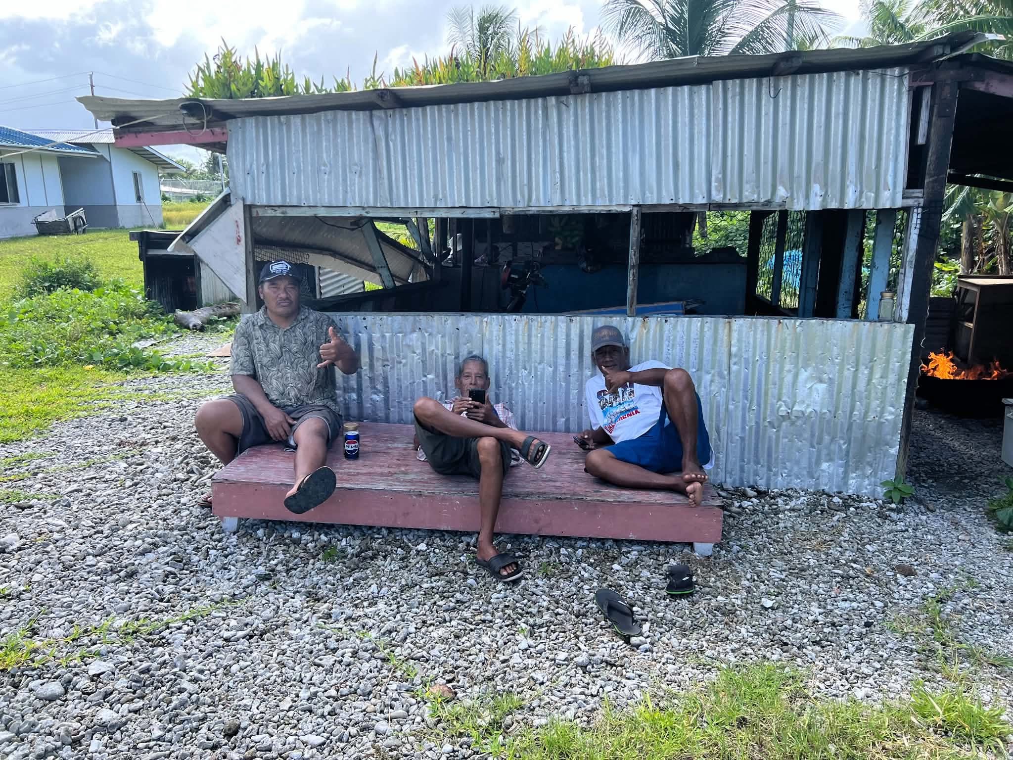 Kili Island, Christmas 2025 — three men seated on a bench outside a tin-roofed building