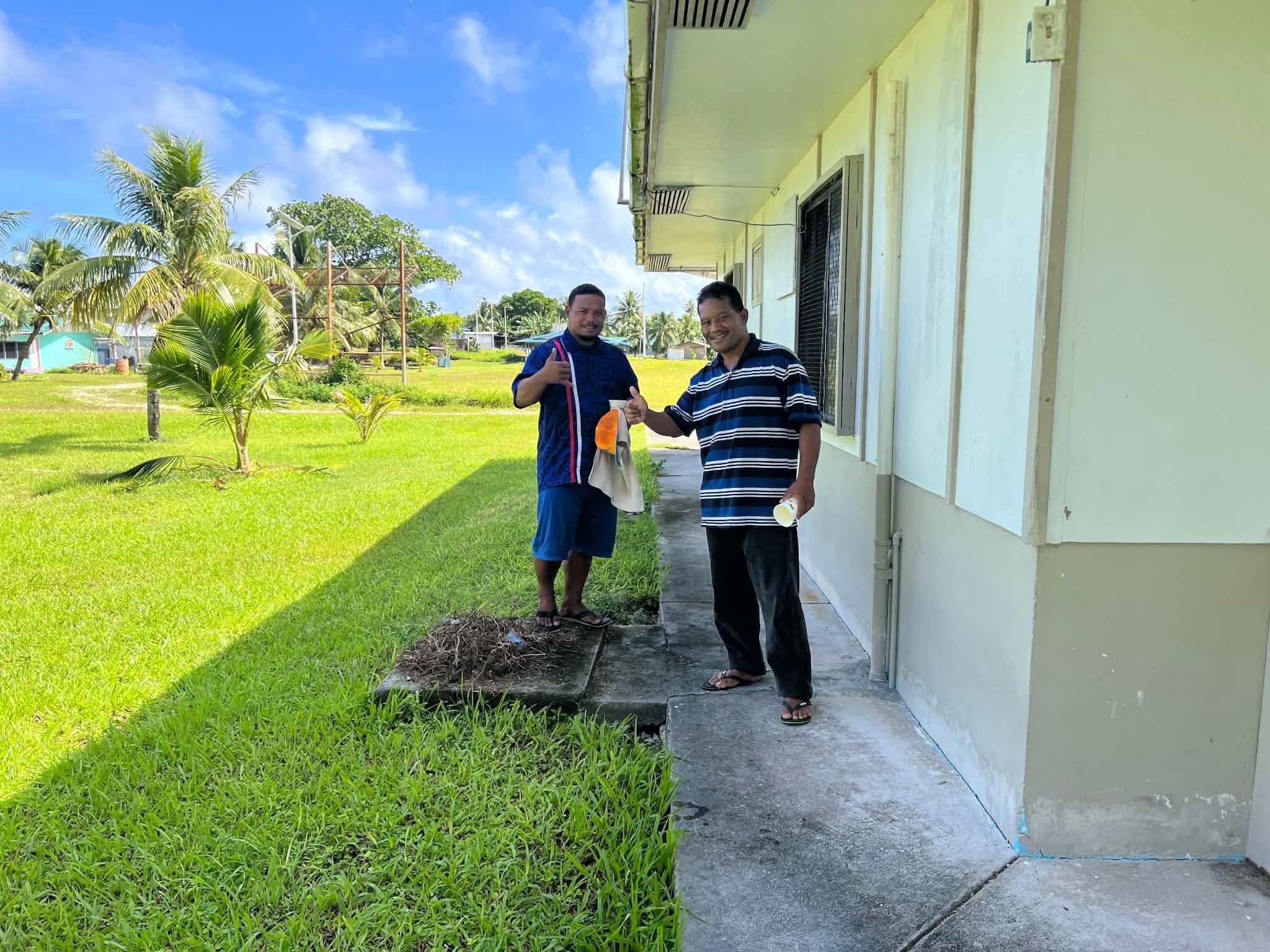 Kili Island, Christmas 2025 — two men giving a thumbs-up outside a building