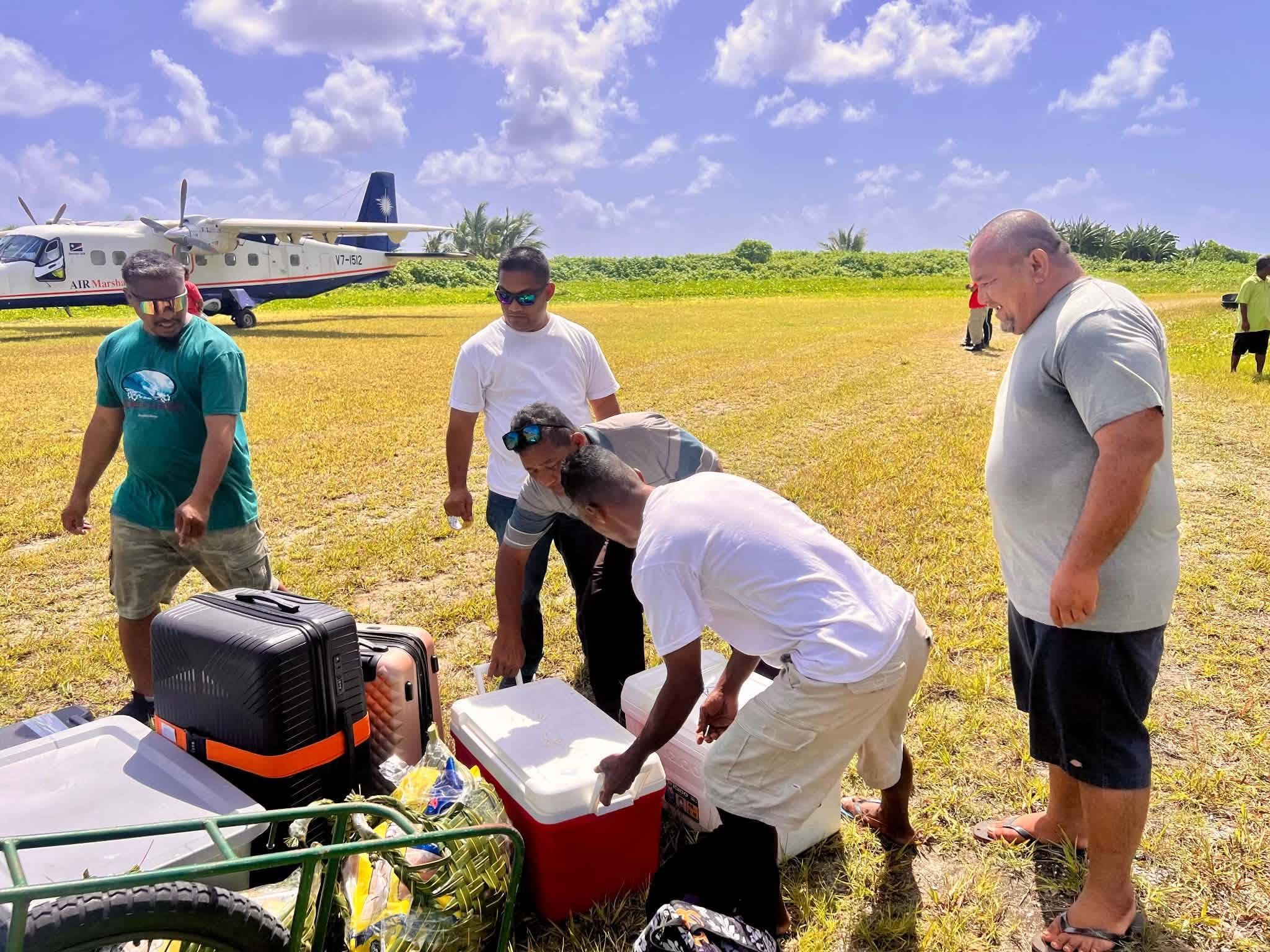 Kili Island, Christmas 2025 — travelers and luggage beside an Air Marshall Islands plane on the airstrip
